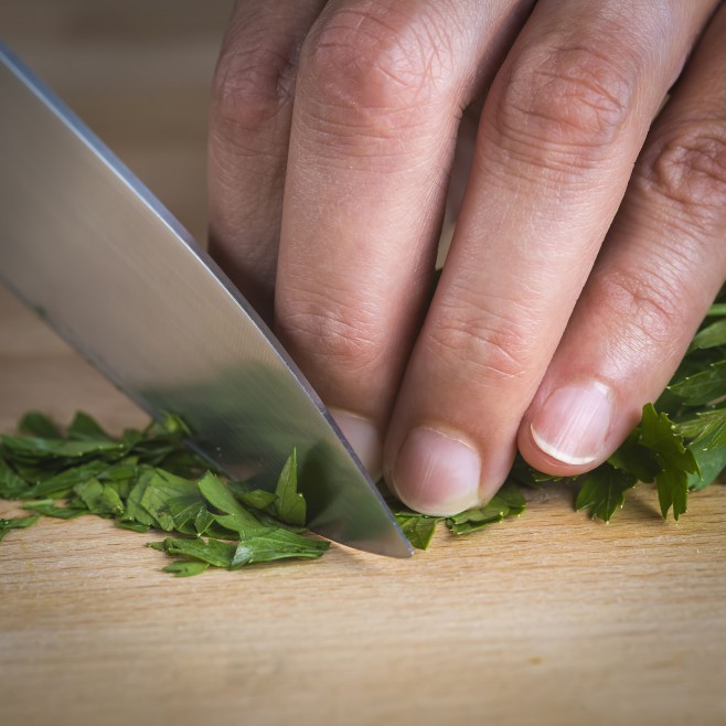 Chef chopping parsley leaves with a knife on a cutting board